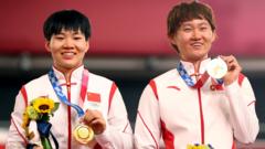 钟天使（右）、鲍珊菊（左）站在颁奖台上展示其奥运金牌（2/8/2021）