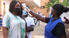 Un scrutateur vérifie la température corporelle des électeurs dans des mesures de coronavirus (Covid-19) alors qu'ils arrivent pour voter dans une université du Wisconsin lors des élections générales ghanéennes de 2020 à Accra, au Ghana, le 7 décembre 2020.