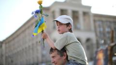 Ukrainian boy on father's shoulders holding a Ukrainian flag and a flower