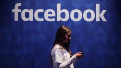 A woman uses her phone under a logo of the social media giant Facebook