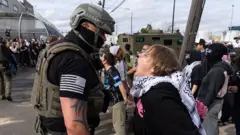A woman shouts at an ICE agent outside the facility.