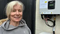 Julie Clague stands next to the battery system at the back of her home.