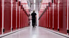 AFP via Getty Images A worker at a data center in Sydney, Australia, walks between two rows of red-faced computer servers