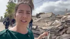 Vanessa Silva reporting from Venezuela showing destroyed buildings behind her