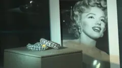 Sparkling earrings sit in a glass case in front of a portrait of Marilyn Monroe