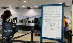 A hand-written whiteboard details the cancellations to trains, in the customer ticket office. On the right there is a sign that says Entry, behind which passengers are waiting to go to the counter.