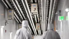 Bloomberg via Getty Images Workers wearing cleanroom suits walk beneath Automated Material Handling System (AMHS) vehicle robots moving along tracks on the roof inside the GlobalFoundries semiconductor manufacturing facility in Malta, New York, U.S., Tuesday, March 16, 2021.