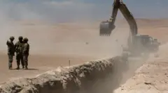 Members of the Chilean army stand near a trench dug by heavy machinery in the desert.