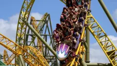 People in a purple rollercoaster race down a yellow track. There are loops and twists on the track behind them.
