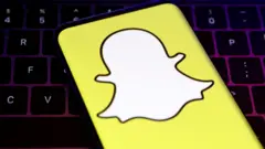 A closeup of Snapchat's logo, a white cartoon ghost with a bright yellow background, held over a laptop conputer keyboard.