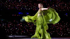 Getty Images Taylor Swift in a flowing green dress during her Eras Tour on stage