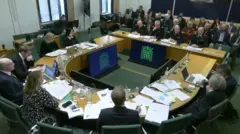 Chief Constable of the House of Commons Craig Guildford sat before the select committee in the House of Commons. He is joined by other officials who are facing eight MPs around an oval table.
