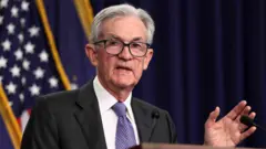 Reuters A man wearing a suit speaks in front of a podium. An American flag hangs in the background.