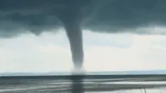A waterspout seen over water with huge clouds forming above.