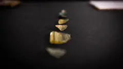 Kevin Church/BBC News Several fragments of glass arranged in a straight line on a dark surface. They vary in size and shape, and some having a yellow tint and others a green and blue hue. One shard is finely etched with a pattern.