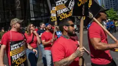 line of picketing workers holding up signs announcing a strike in front of NYC skyscraper