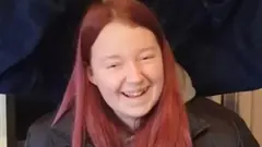 Teenage girl with pink care and black jacket. She is smiling at the camera. 
