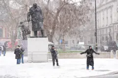 PA Media people dance in the snow in front of the statue of Winston Churchill in Parliament Square, Westminster.