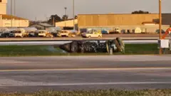 The smoking remains of an engine sitting on the grass next to the runway at Louisville International Airport.
