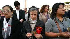 Durante o terço em homenagem ao Papa Francisco, uma devota segura contas de oração e uma vela.
