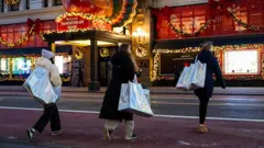 Bloomberg via Getty Images Three shoppers carry large shopping bags while crossing the street, in front of a Macy's store decorated with holiday lights.