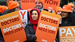 Getty Images Participants hold placards outside Bristol Royal Infirmary hospital on the first day of a five day resident doctors strike, on December 17, 2025 in Bristol, England.