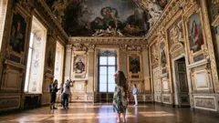 A visitor takes a picture in the Apollo Gallery during its reopening at the Louvre Museum