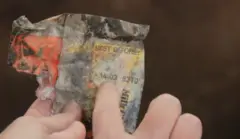 A hand holding a old chocolate biscuit wrapper, pointing to the best before date which says 14 03 83 on it