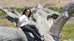 Teenage girl sat on a fallen tree with sun-bleached bark.