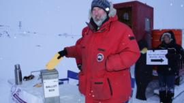 A man in a red coat votes in the snow at an outdoors polling booth