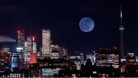 A moon rising over a city at night