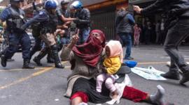 A woman hangs onto her baby as police clash with foreign nationals staging a sit-in protest