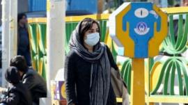 A woman wearing a face mask walking down a street in Iran