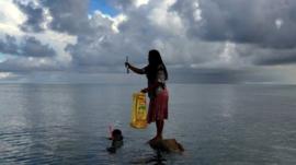 Woman stands on rock in the sea off Kiribati island