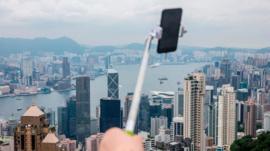 A tourist holds a selfie stick (C) from the peak which overlooks the city of Hong Kong and Victoria Harbour on June 9, 2018