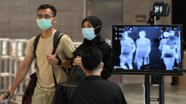 A couple, wearing protective facemasks amid fears about the spread of the COVID-19 novel coronavirus, walk past a temperature screening check at Changi International Airport in Singapore on February 27, 2020