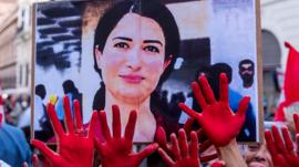 Image of Hevrin Khalaf held up during a protest with people showing hands covered in red paint