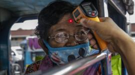 An elderly woman riding a passenger jeep has her temperature checked at a checkpoint in Manilla