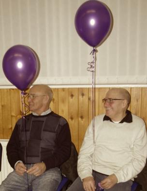 Two granddads' hold purple balloons as they sit and smile