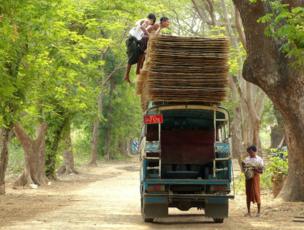 Two men pile fencing panels on the roof of an open-back bus