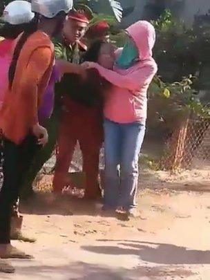 Hai cảnh sát và một phụ nữ đeo khẩu trang lôi kéo một người dân trong một clip