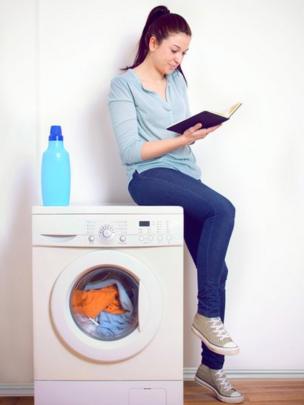 Una persona leyendo un libro apoyada en una lavadora.