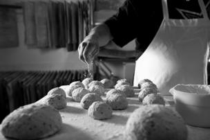 A baker sprinkles flour over bread rolls