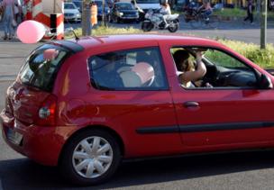 A red car is full of passengers and balloons