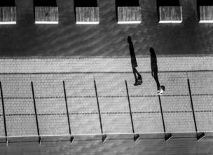 Black and white aerial photo of two people walking in the street, casting large shadows