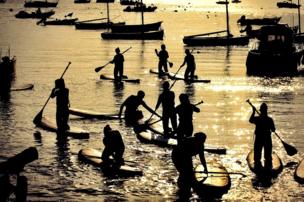 Paddle boarders sail as the sun sets and reflects on the water