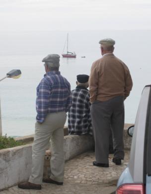 Three men watch a boat sail by, a dog pops out from under one of the men's leg