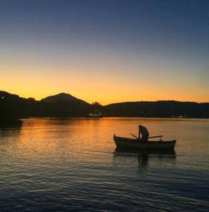 A fisherman sails on a calm sea as the sun sets