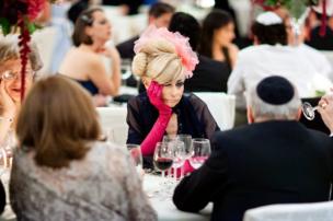 A woman attending a wedding. wearing in a fascinator and pink gloves she holds her face in disappointment