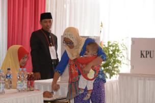 Seorang pemilih, sambil menggendong anaknya, mencelupkan jarinya ke dalam tinta sebagai tanda telah memberikan hak suaranya